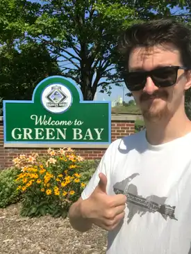 Me in front of the Welcome to Green Bay sign, giving a thumbs up while wearing sunglasses